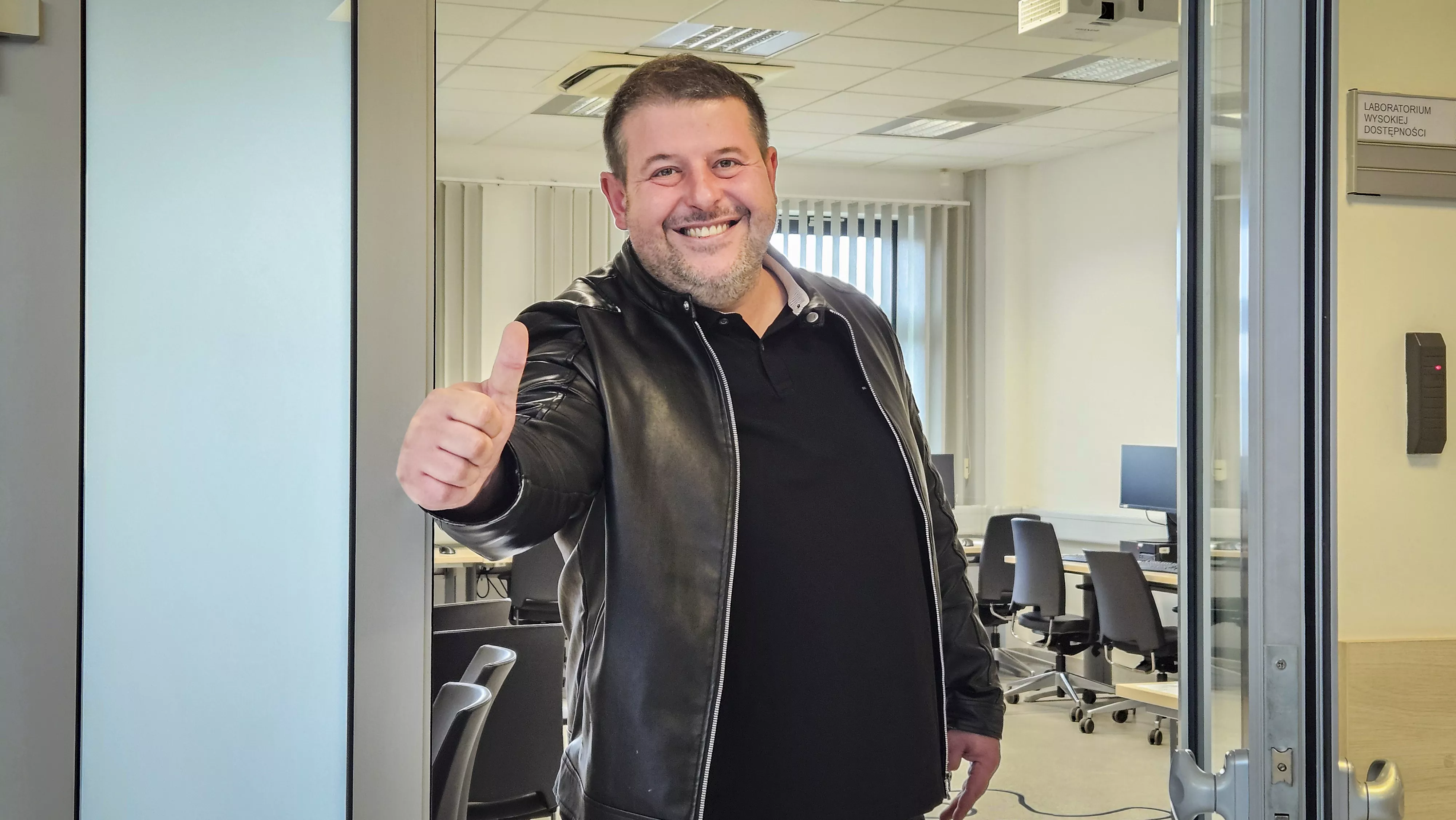 Zadowolony uczestnik Warsztatów unosi kciuk w górę i uśmiecha się do kamery